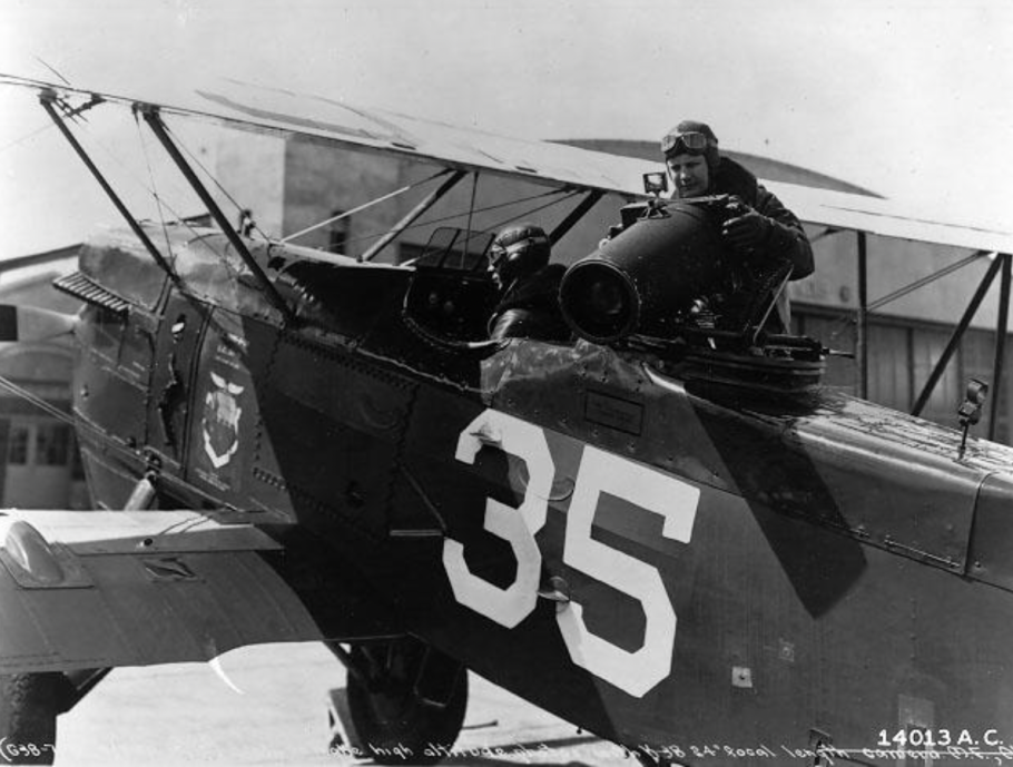 A black and white picture of a plane with a 35 on the side. Two people are in the plane, one pilot and one holding a large camera. 