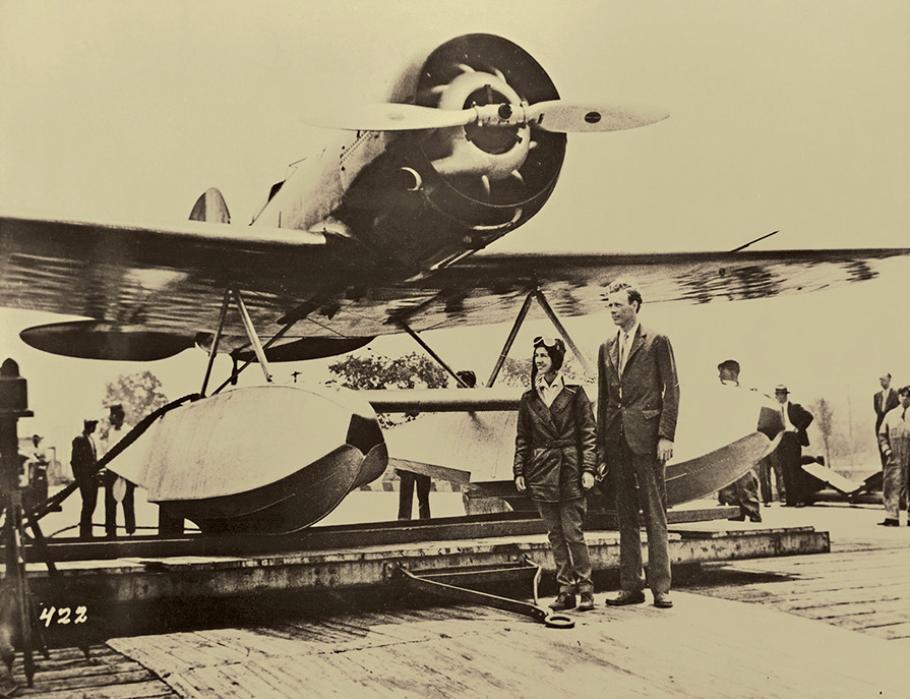 Anne Morrow Lindbergh and Charles A. Lindbergh pose in front of their airplane, a Lockheed Model 8 Sirius, a small airplane with a propellor.