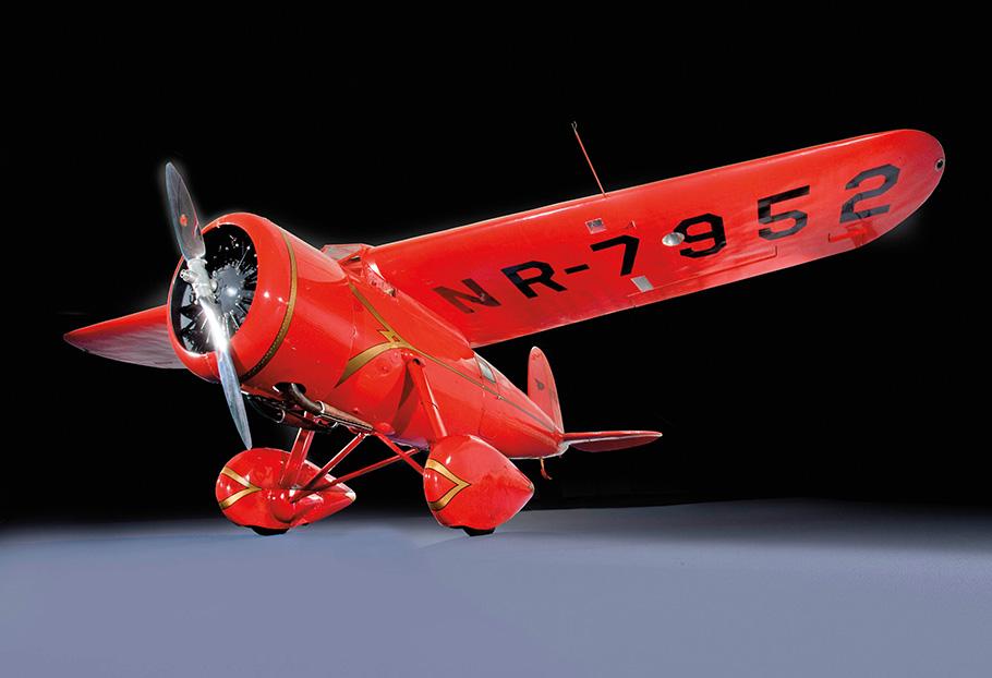 Three-quarter right front view from low angle of Amelia Earhart's Lockheed Model 5B Vega, a small red airplane with a propellor..