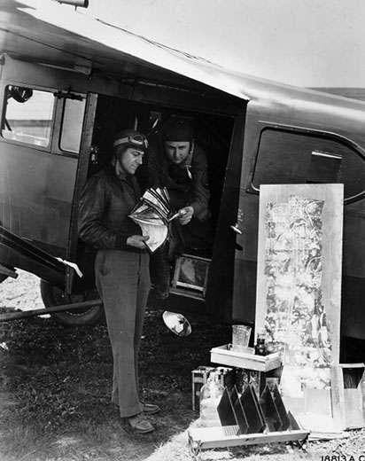 Two men stand in the door of a plane looking at photography equipment. 