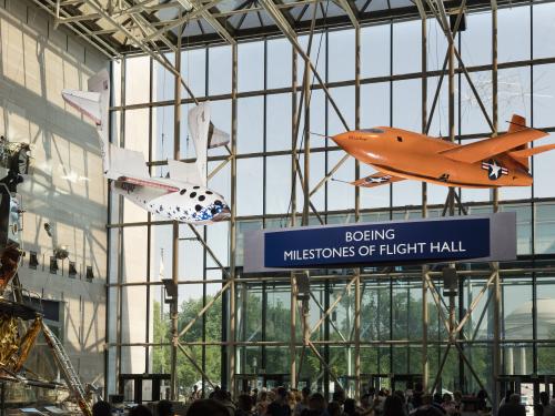 Two airplanes hang from the ceiling in front of a glass wall that has the name "Boeing Milestones of Flight Hall."