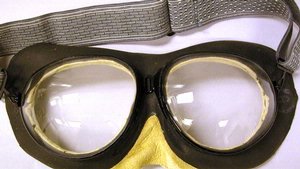 Goggles with dark brown leather around glass lenses and yellow leather around the eye and nose pieces.