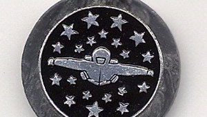 Silver and black keychain showing a figure in a space suit surrounded by stars.