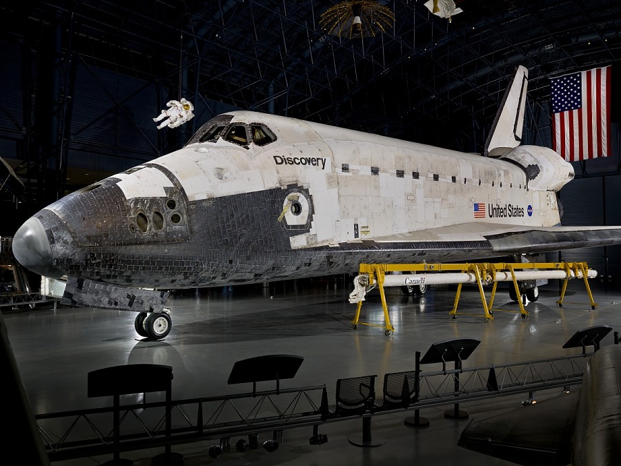 Space Shuttle Discovery displayed in a hangar with the United States flag in the background.