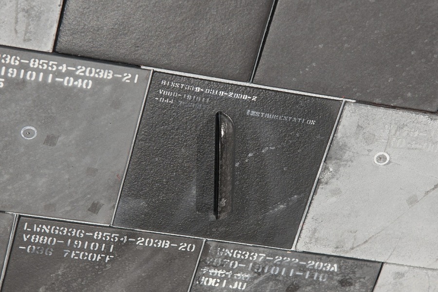 A close-up of several dark tiles with embossed alphanumeric codes and a single metallic handle, suggesting a system of organization or identification, possibly for inventory or categorization purposes.