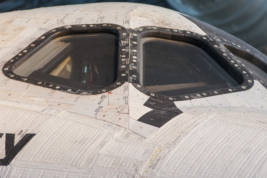 A close-up view of the cockpit windows of a space shuttle, highlighting the thermal protection tiles around the windows designed to withstand extreme temperatures during re-entry into Earth’s atmosphere.