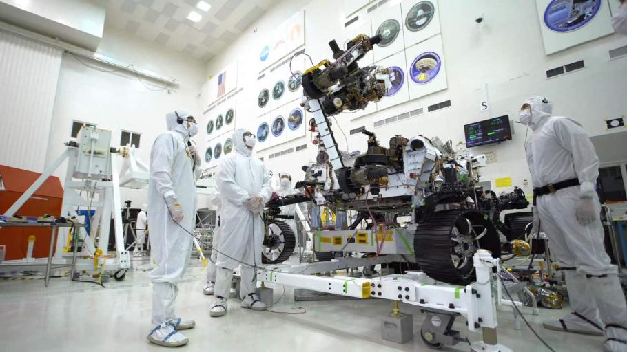 Three people in white protective suits work on rover