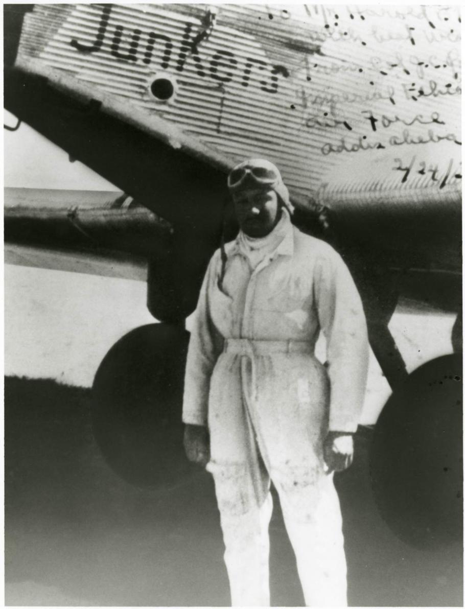 A black and white photograph of a man standing in front of a plane.