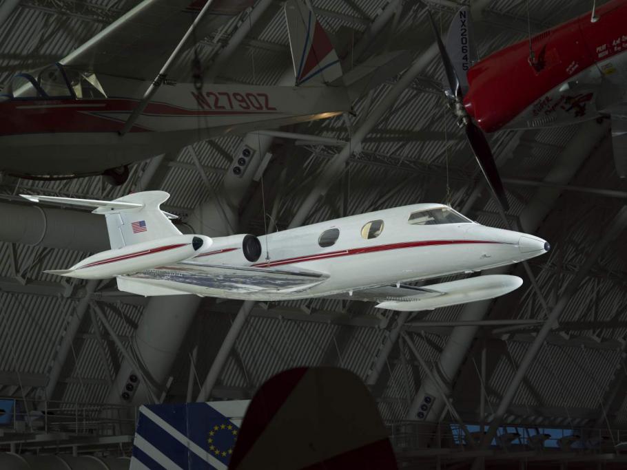 White, twin-engine business jet with red stripe and metallic wings, hanging in dim interior