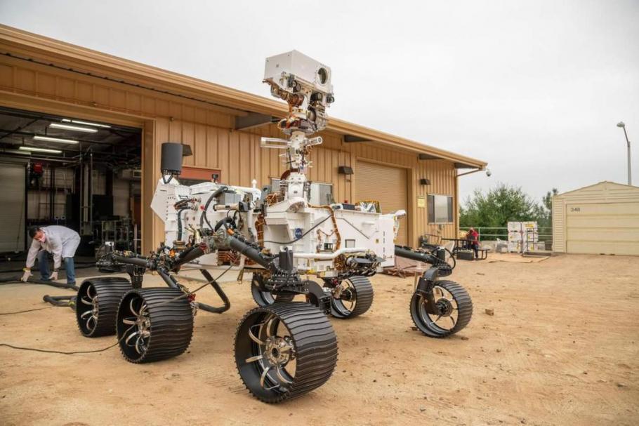 A car sized rover with six wheels sit outside a garage.