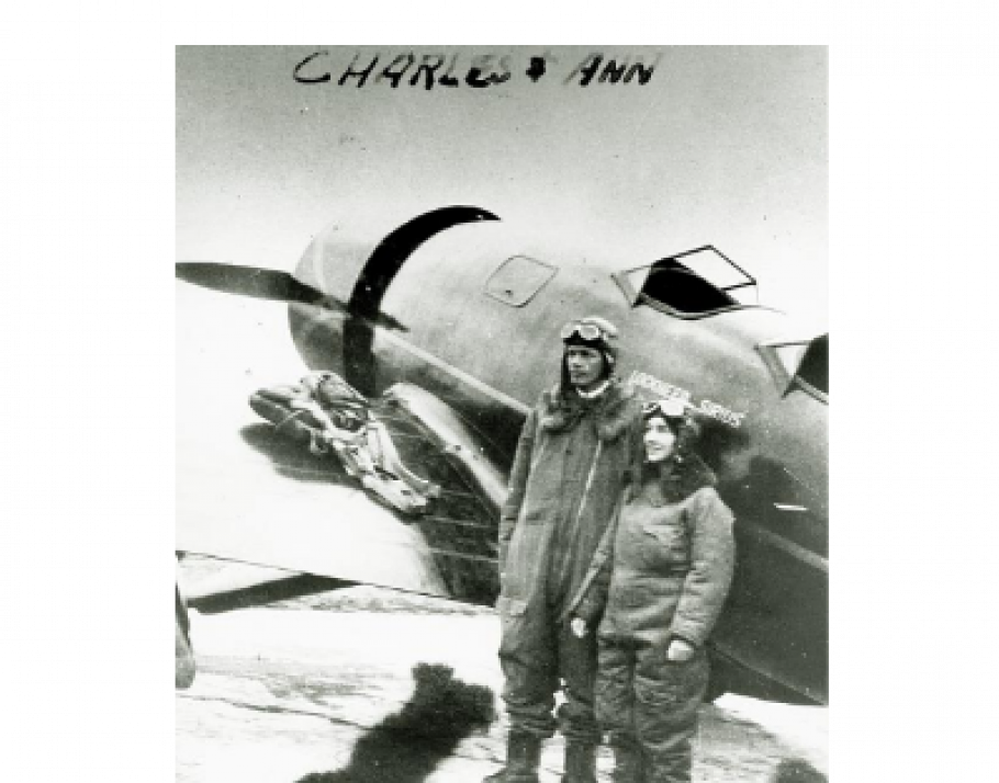 Charles and Anne Lindbergh stand on side of their Lockheed Sirius while wearing aviator gear.