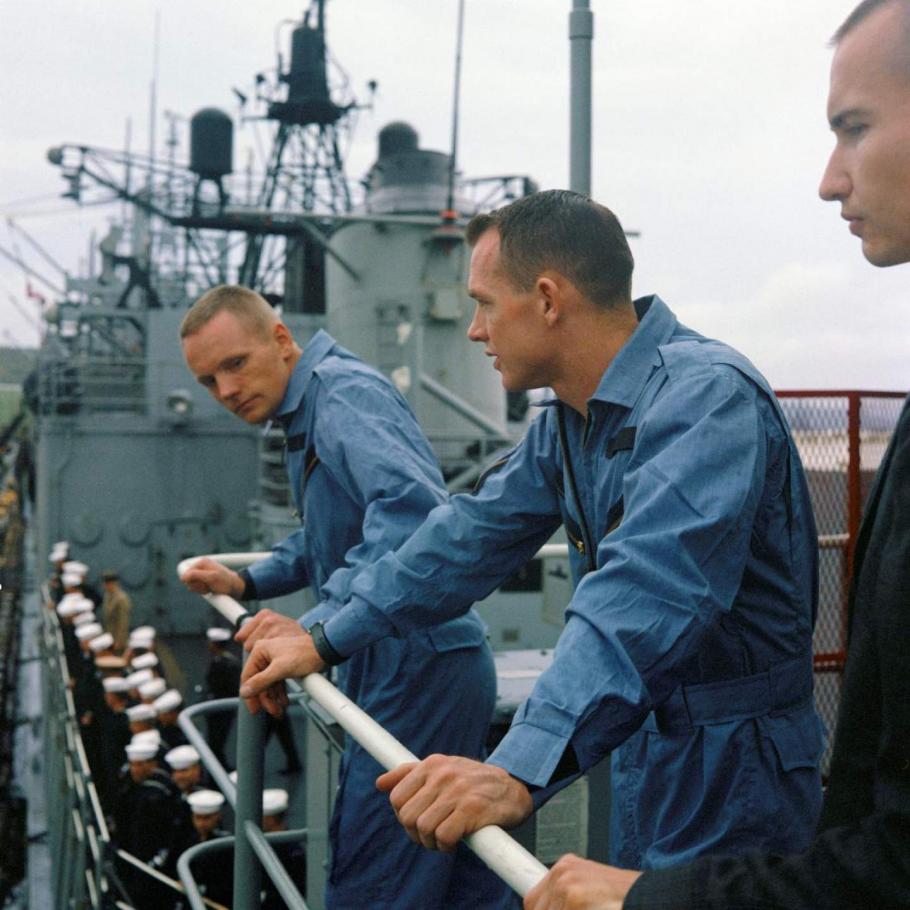 Three white men lean over the railing of a ship.