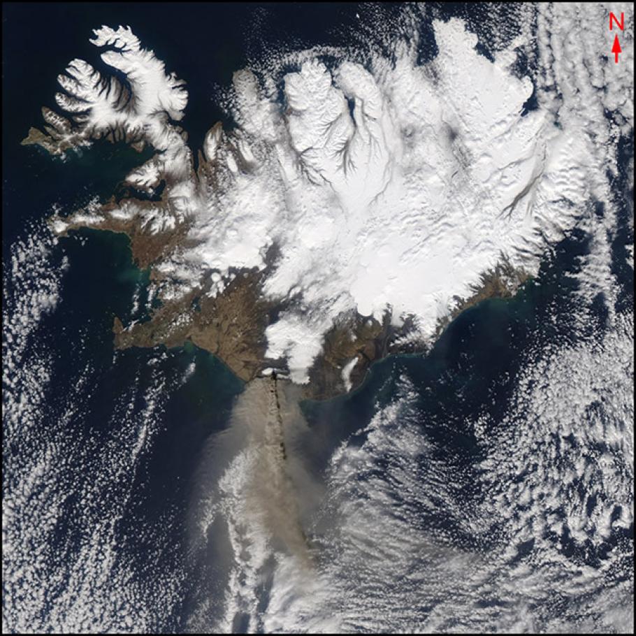 Satellite image of an island that is mostly covered in ice and snow. Plumes of smoke and ash can be see to the south.