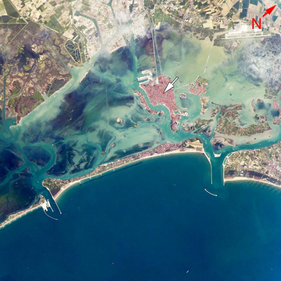 Satellite image of a city in Italy that is entirely surrounded by water. A larger land mass can be seen in the top of the image.