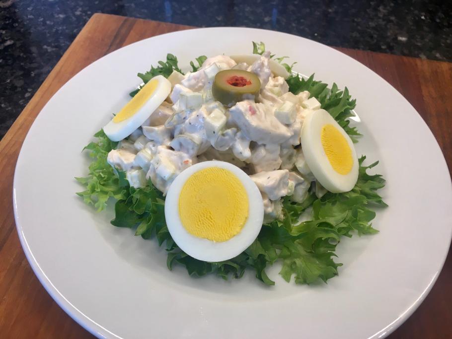 Photograph of chicken salad on white plate with a bed of lettuce, hard boiled egg cut in half, and green olives