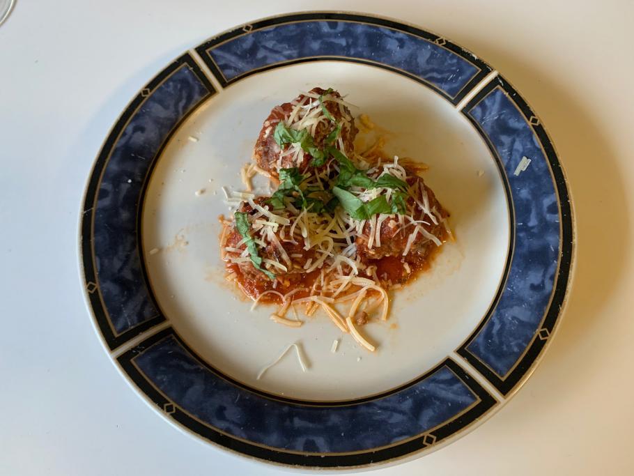 Three meatballs covered in red sauce, topped with shredded cheese and green shredded basil on a white place with a blue border