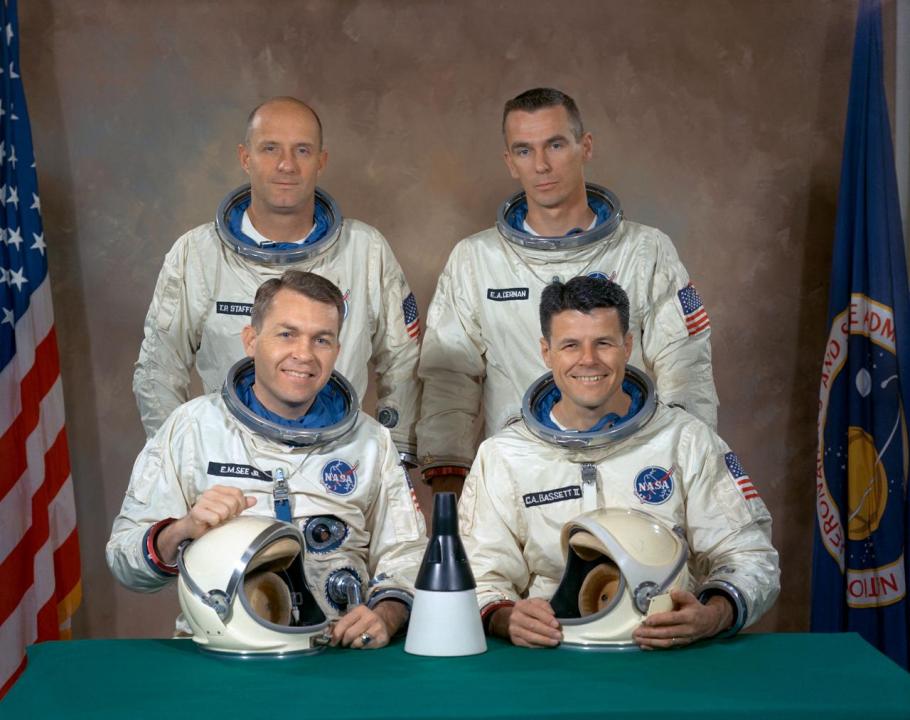 four men seated in two rows in spacesuits