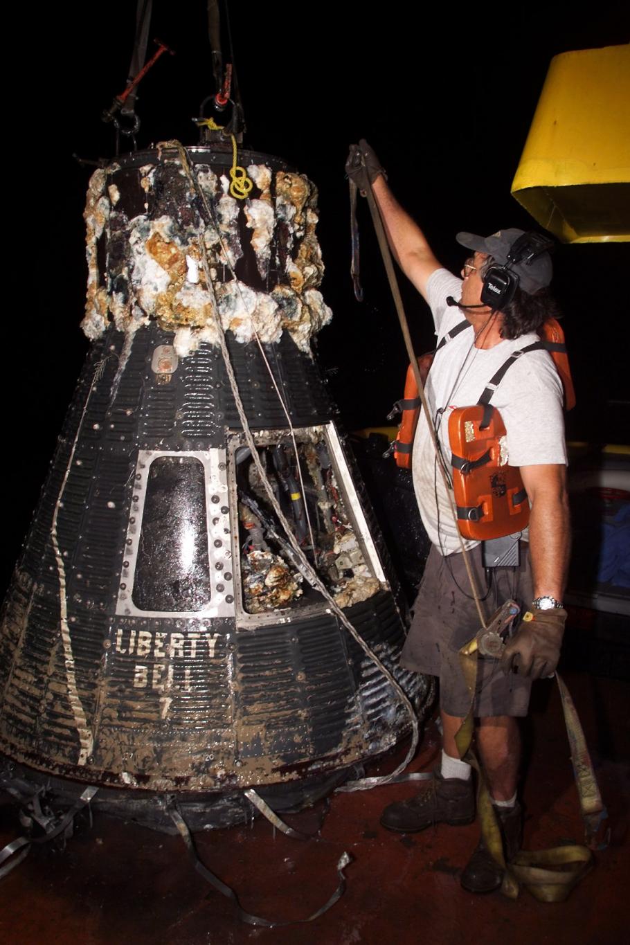 Man stands next to a space capsule recently removed from the ocean