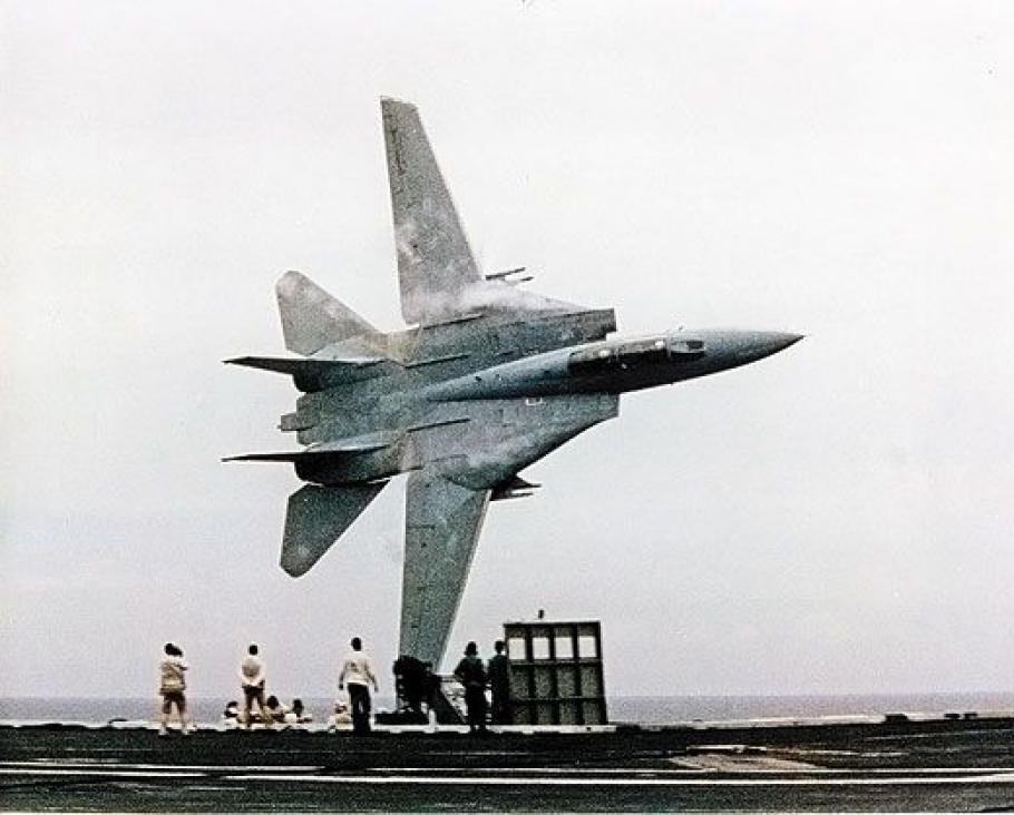 A jet flying sideways over an naval carrier