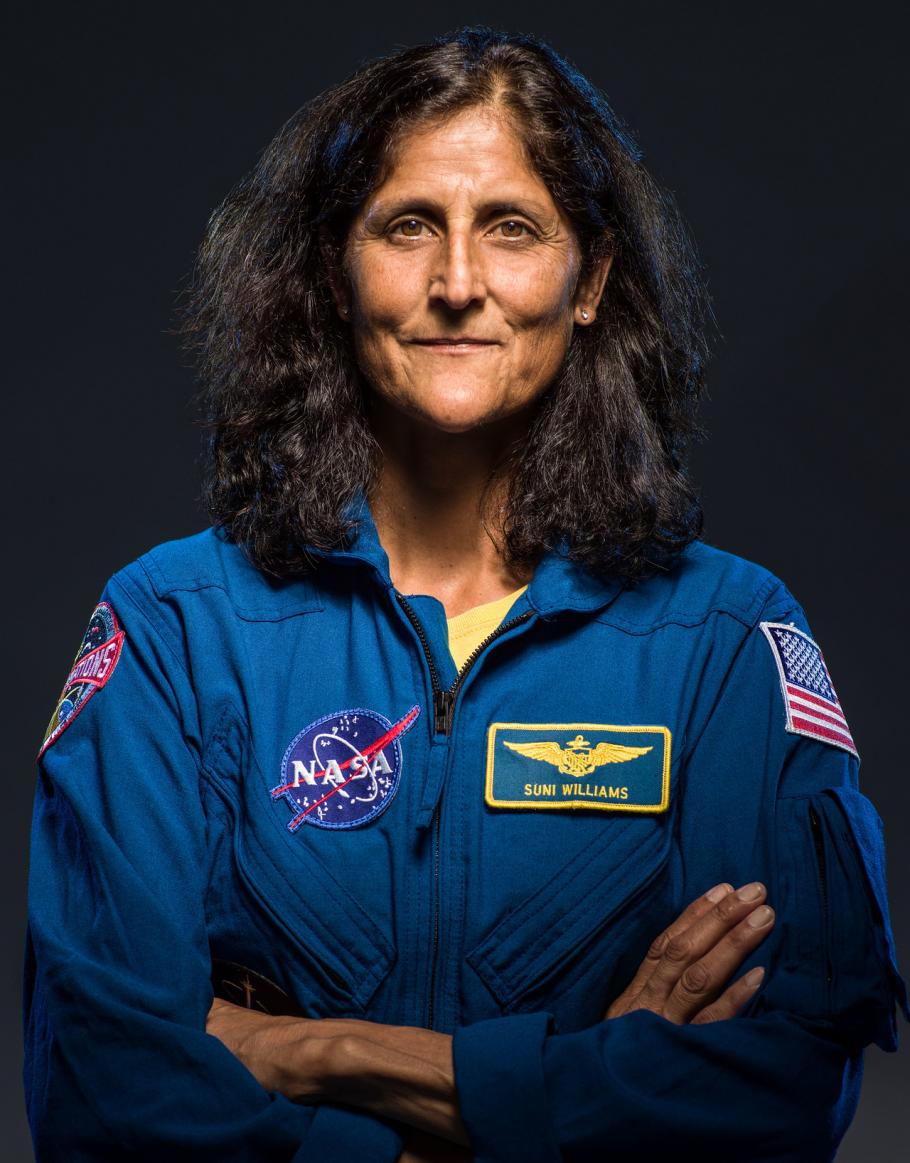 A woman in a flight suit with the name tag Suni Williams. Her arms are crossed. 