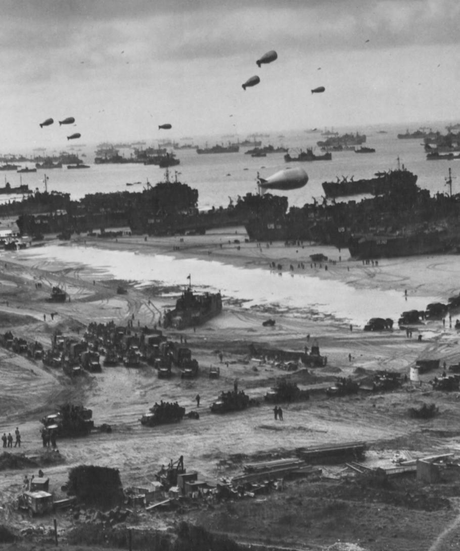 Zepplin shaped balloons float over tanks and more on a D-Day battlefield. 