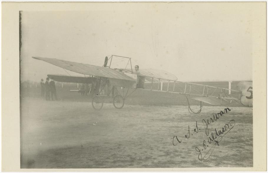 black and white photograph. One-half left rear view of monoplane. man in cap in cockpit. men standing in left background. Number five is marked on the tail of the aircraft