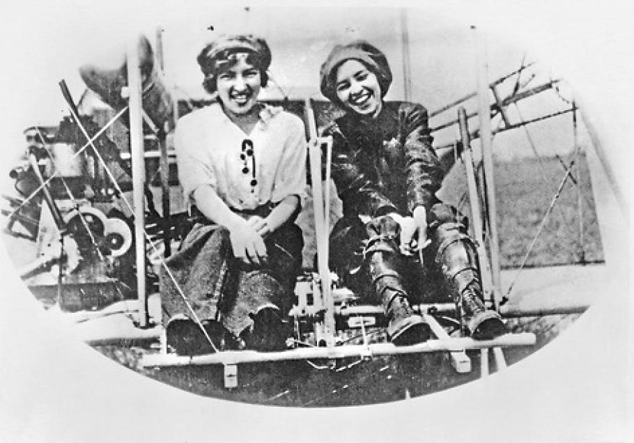 Two sisters sit in an airplane, laughing and smiling.
