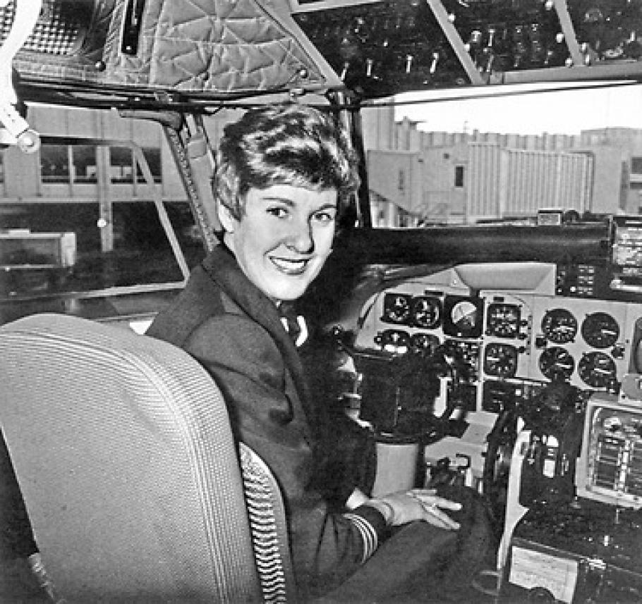 A woman turns around and smiles from the cockpit of a plane.