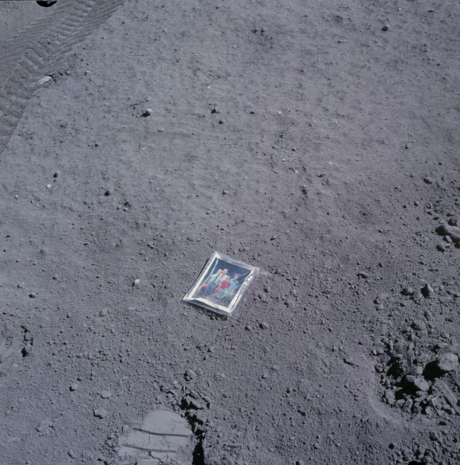 A photo of a framed photo of a family laying on the surface of the Moon.