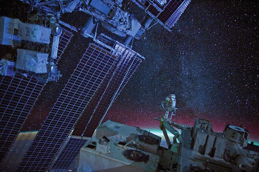 Starry sky above earth with ISS solar panels in the foreground.