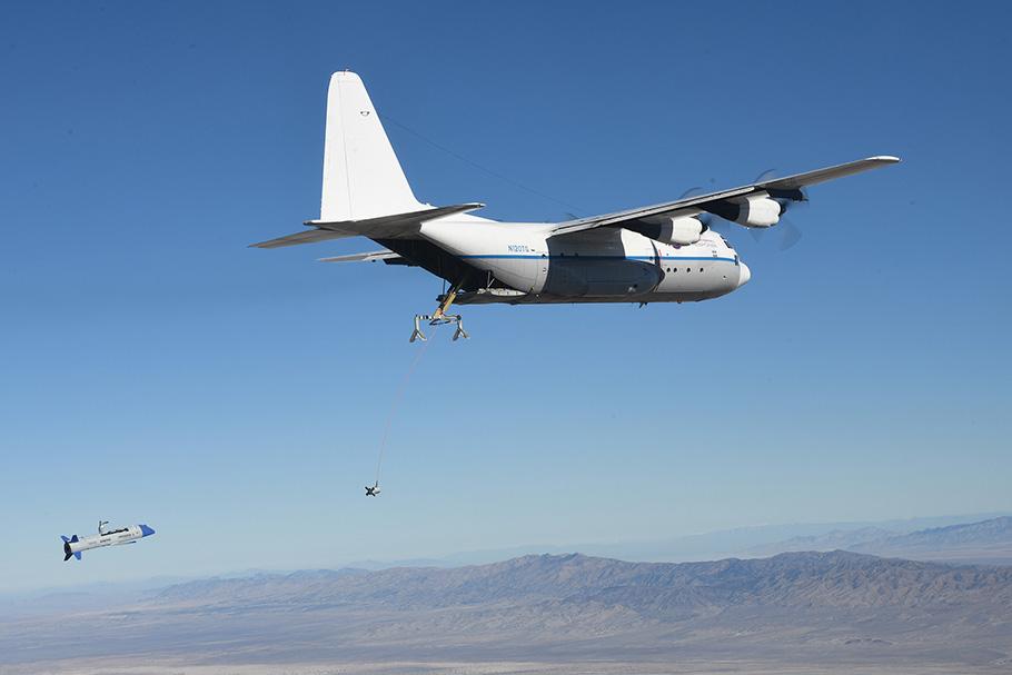 C-130 Hercules plane flying over the desert above a drone.