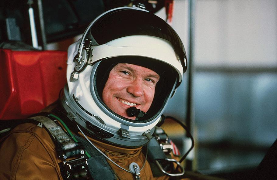 A man in a rounded space-like helmet smiles at the camera. 