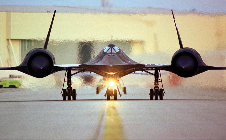 A black plane with three rounded bumps speeds down a runway. The heat and speed is evident in the photo. 