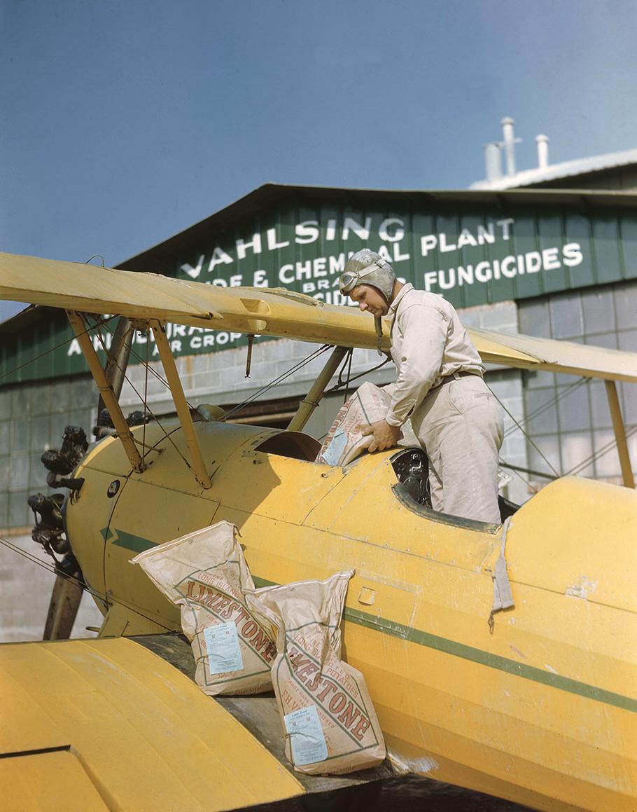 A pilot pours a bag labelled limestone into a cavity on his airplane. 