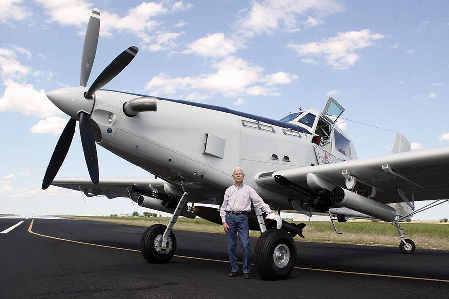 A man stands in front of a large airplane with a propeller. 