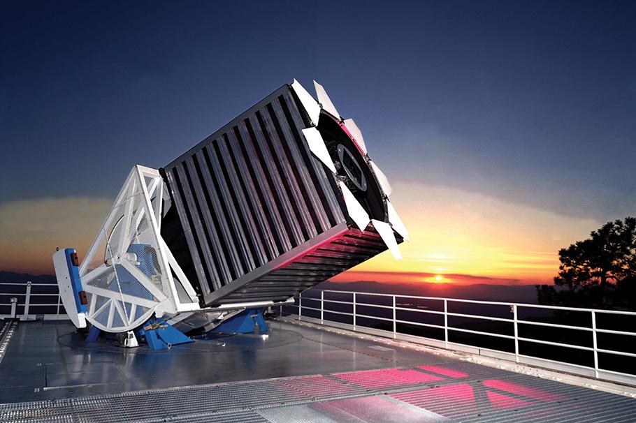 A large telescope pointed upward as the sun sets in the background. 