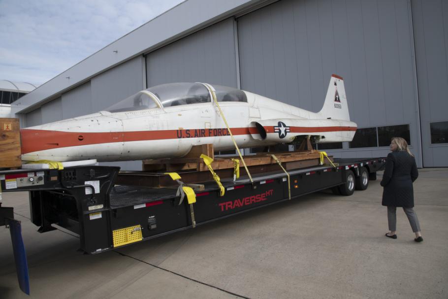 A woman examines a T-38 Talon aircraft while it's strapped to the back of a truck without its landing gears.