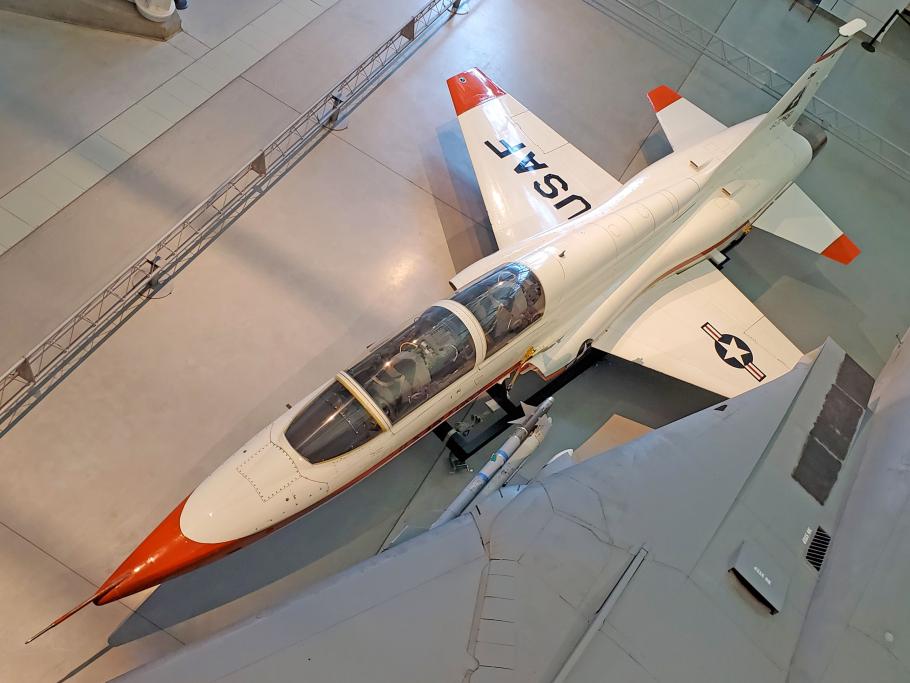 A white T-38 Talon aircraft with orange on the tip of the edges view from a top angle.