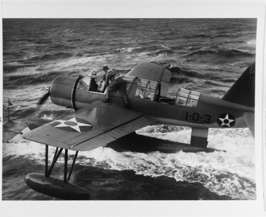 Black and white image of an airplane riding on top of water with a man on its wing.