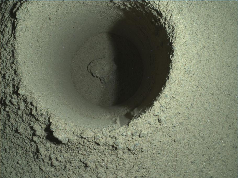 A circular hole in the soil of Mars with smooth sides indicating it was created by a mechanical instrument.