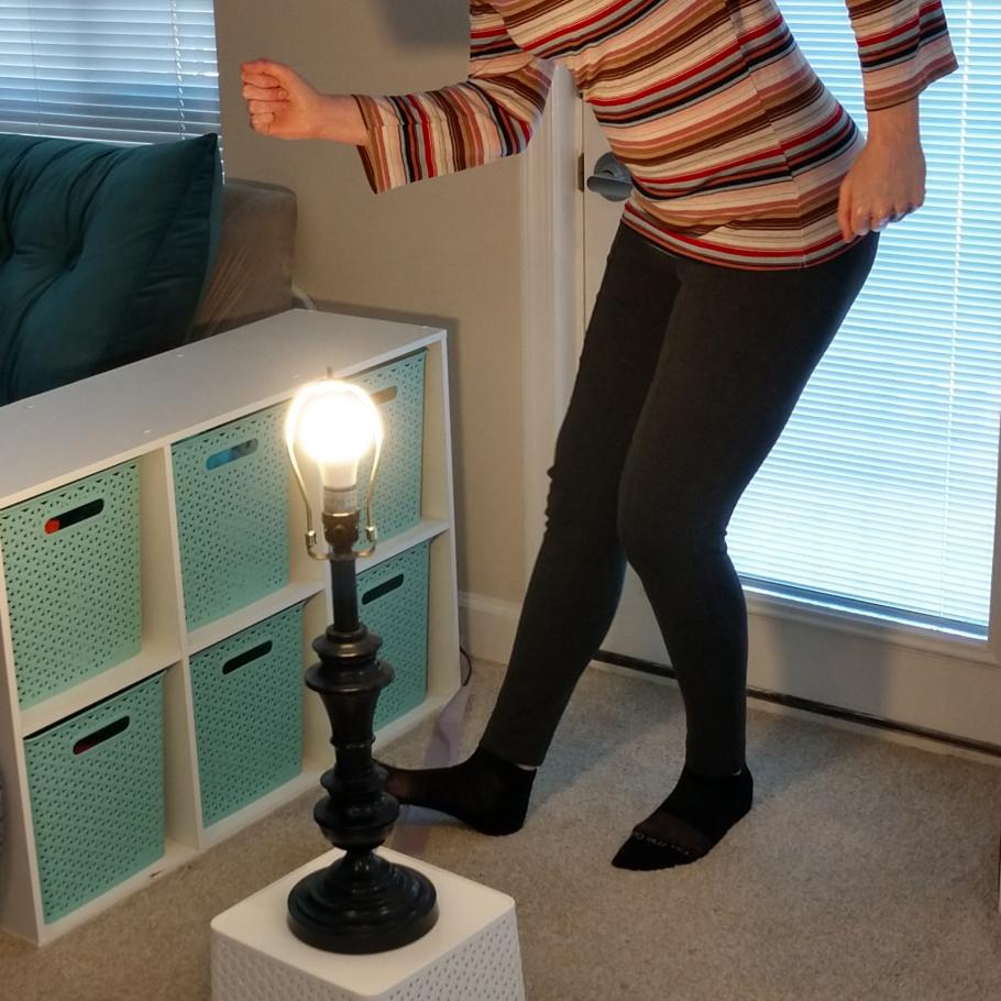 A person dances around a lamp with the lampshade off and the bulb revealed.