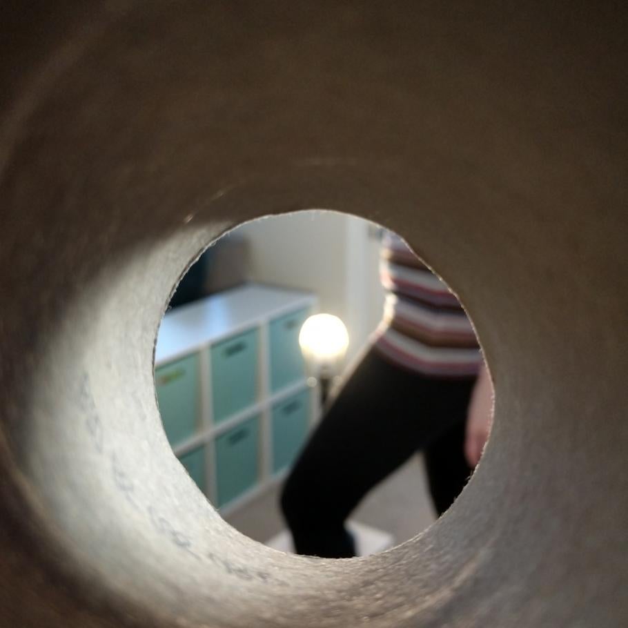 A person dancing around a lamp with the lamp shade removed, as seen through the end of a tube. 