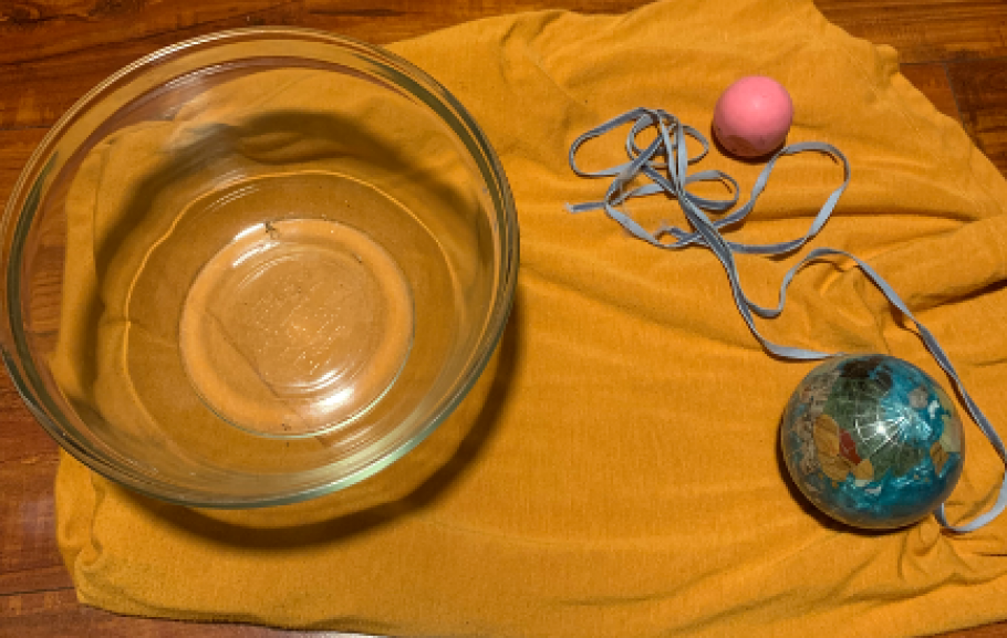 A photograph of supplies for an activity including a bowl, a ball that looks like Earth, another ball, a blanket, and a string. 