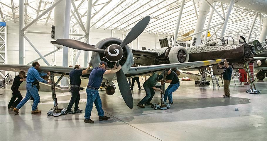 Eight interior workmen pushing a World War II german bomber into position for display.