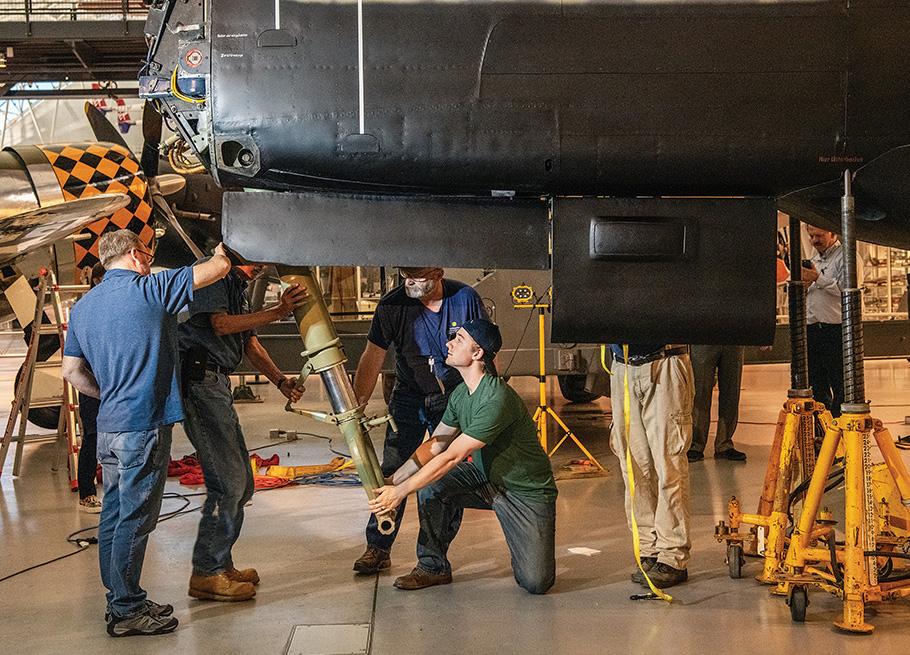 A team of restoration experts positioning landing gear on a WW II aircraft.