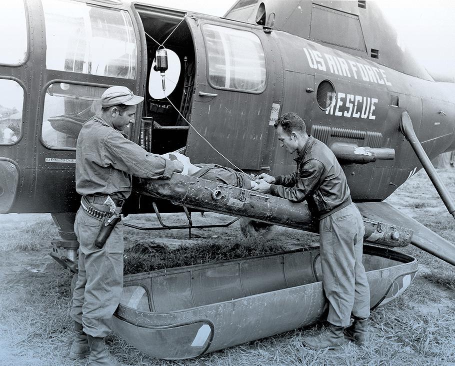 Wounded soldier is loaded on a Korean War era helicopter by two medics.