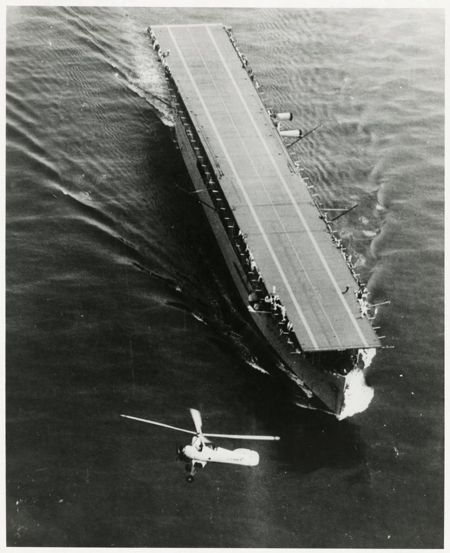 Black and white grainy image of USS Langley in water and an aircraft flying around it