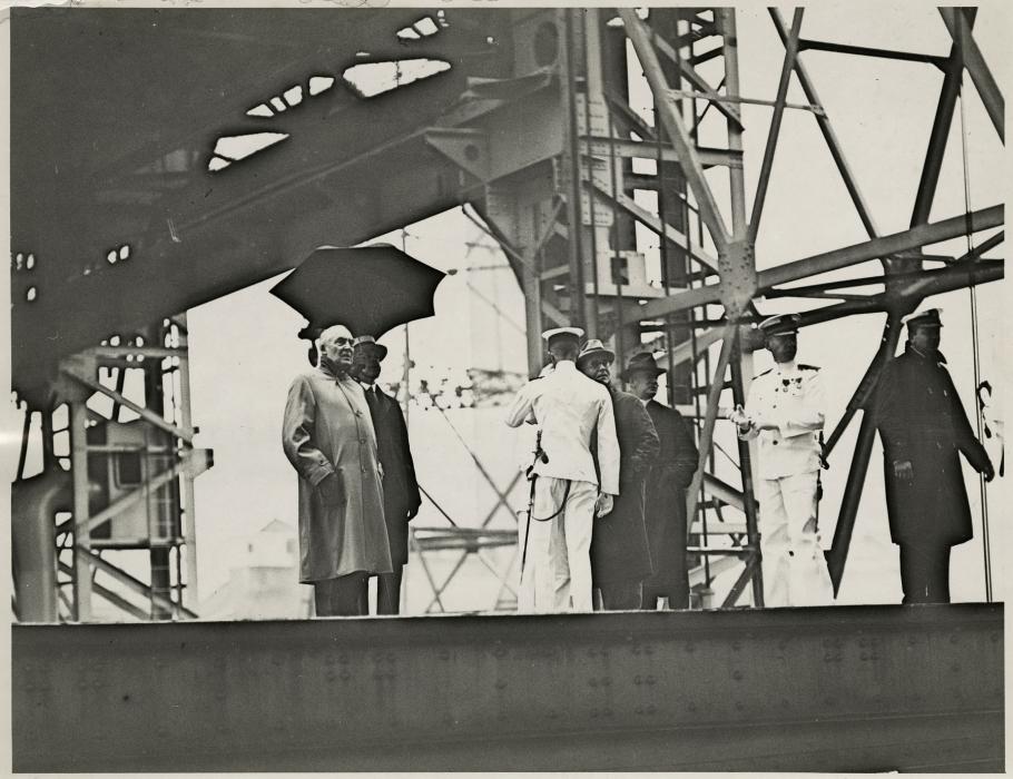 Black and white grainy image of people standing by a steel structure