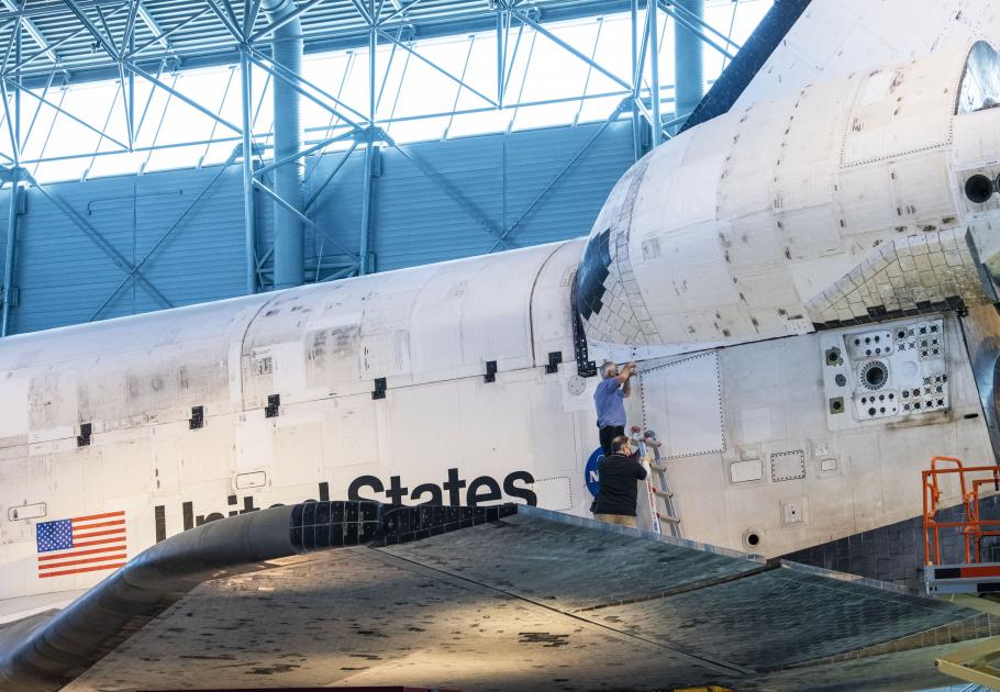 Two individuals opening a hatch from the tail of Space Shuttle Discovery.