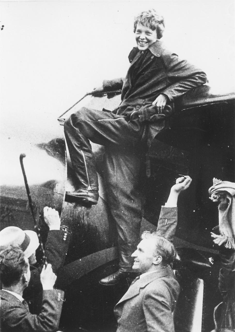 A woman stand by the wing of an aircraft, smiling, while others surround her.